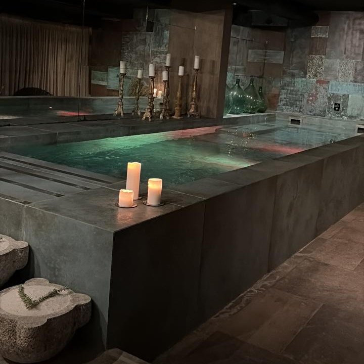 A candlelit plunge pool in a dimly lit spa, with tall candlesticks and glass demijohns beyond