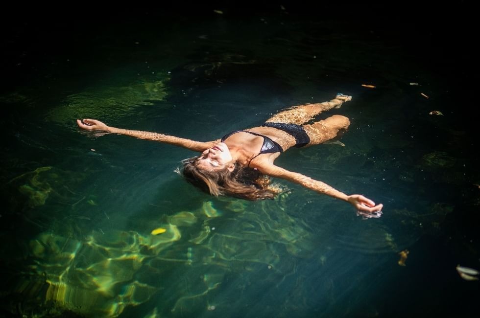 A guest floating on her back, arms outstretched, in the dark green thermal river at Rio Perdido, Costa Rica