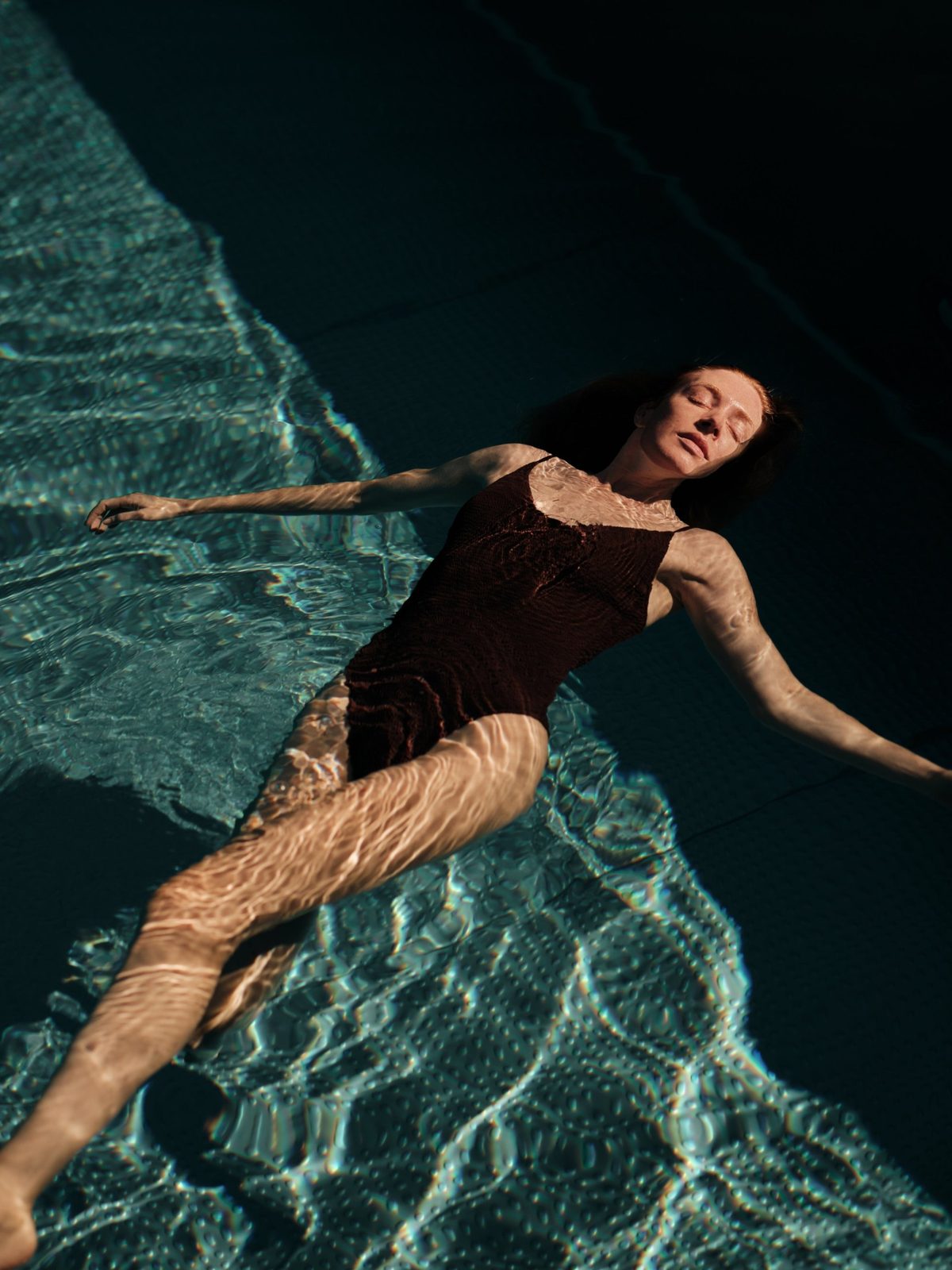 A guest floating on her back in a dark, sunlit pool, Lanserhof