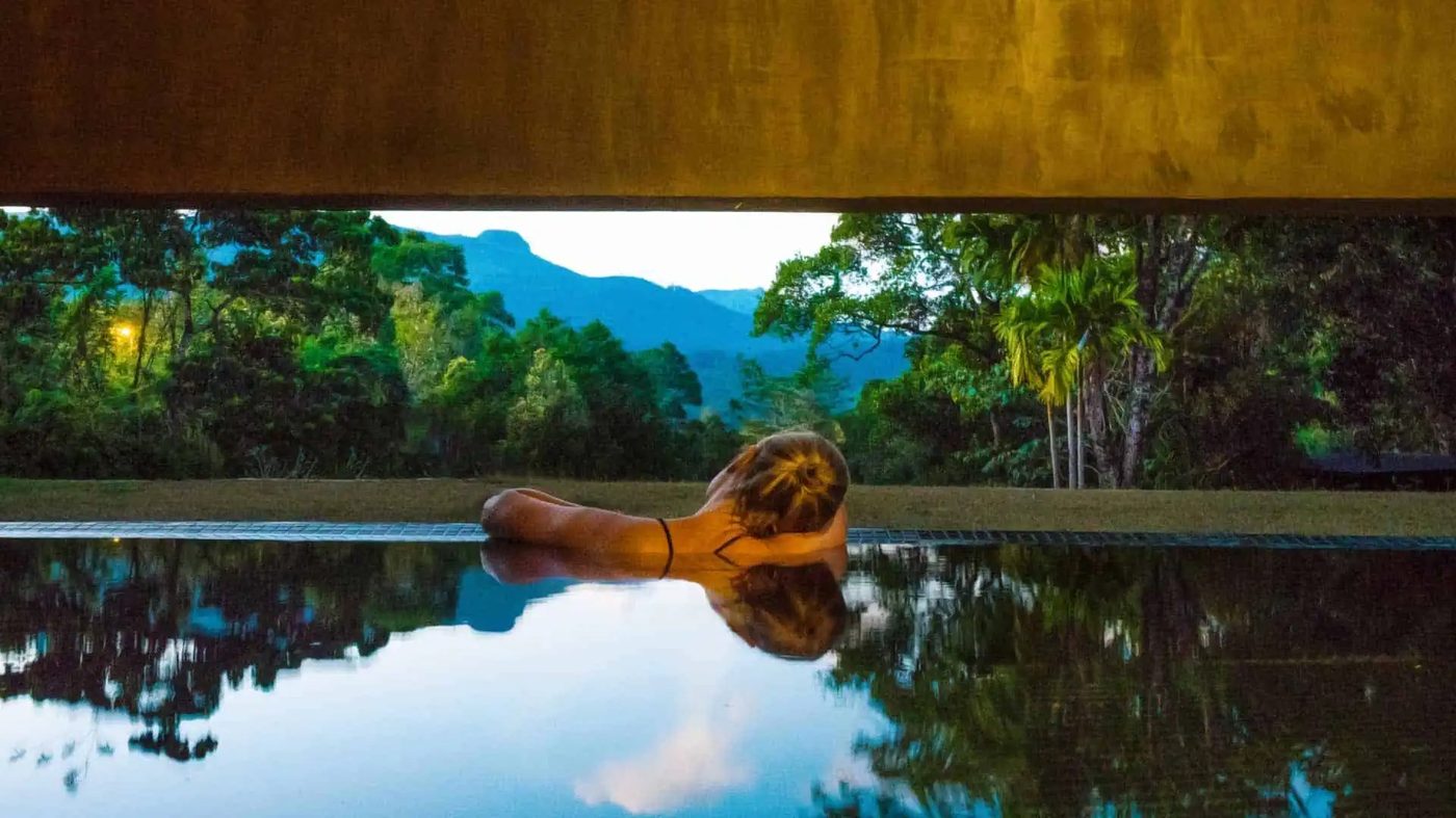 A guest resting at the edge of a still infinity pool in the hills near Kandy, Santani Wellness